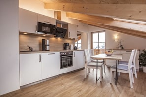 A modern kitchen with white cabinetry, a wooden ceiling, and a dining area with a table and chairs. - Bergblick Buchwieser (Unterammergau)