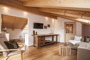 Un salon chaleureux avec un plafond en bois, un téléviseur fixé au mur et un coin salon confortable avec un canapé et un fauteuil.