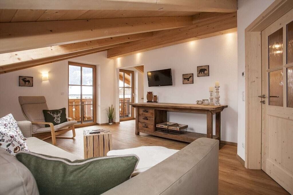 A cozy loft-style living room with a high ceiling, wooden beams, a large window, a television, and a fireplace.