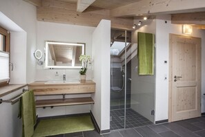 Une salle de bain moderne avec un meuble-lavabo en bois, une cabine de douche en verre et un escalier apparent.