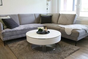 Un salon moderne avec un canapé d’angle gris, une table basse ronde et un tapis gris moelleux.