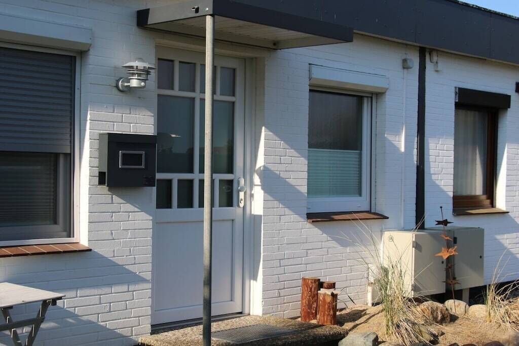 Un edificio de ladrillo blanco con una puerta, ventanas y una pequeña mesa exterior.