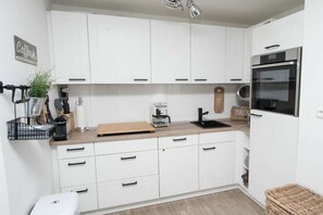 A modern kitchen with white cabinets, a stainless steel oven, and a coffee station. - Holiday apartment with 2 bedrooms (Büsumer Deichhausen)