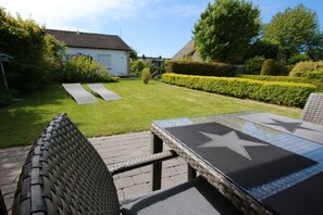 An outdoor patio area with wicker furniture, a star-patterned table, and a well-maintained lawn. - Holiday apartment with 2 bedrooms (Büsumer Deichhausen)