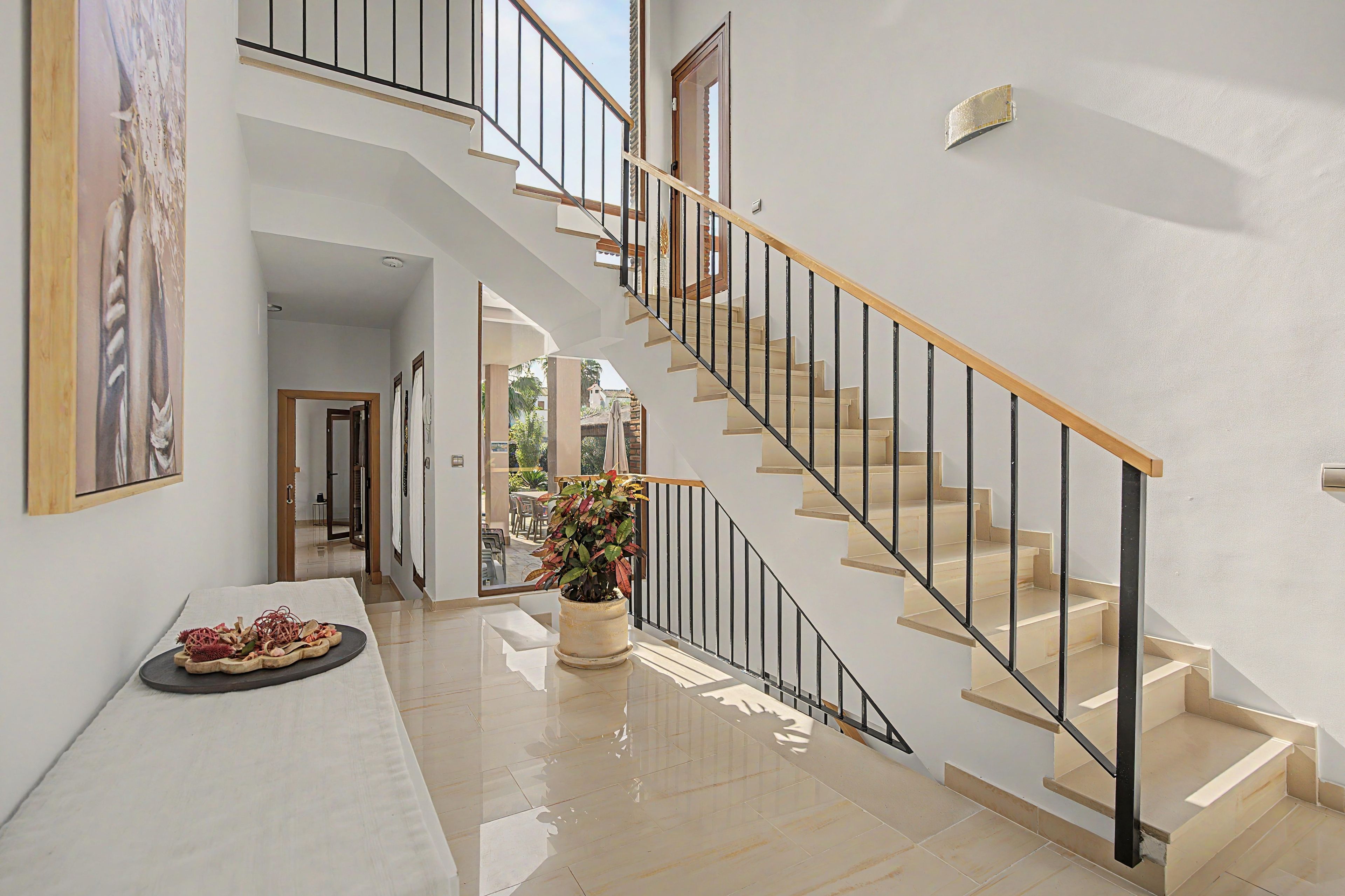 A modern interior with a staircase, a dining area with a table and chairs, and a potted plant.