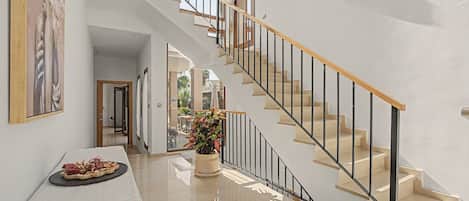 A modern interior with a staircase, a dining area with a table and chairs, and a potted plant.