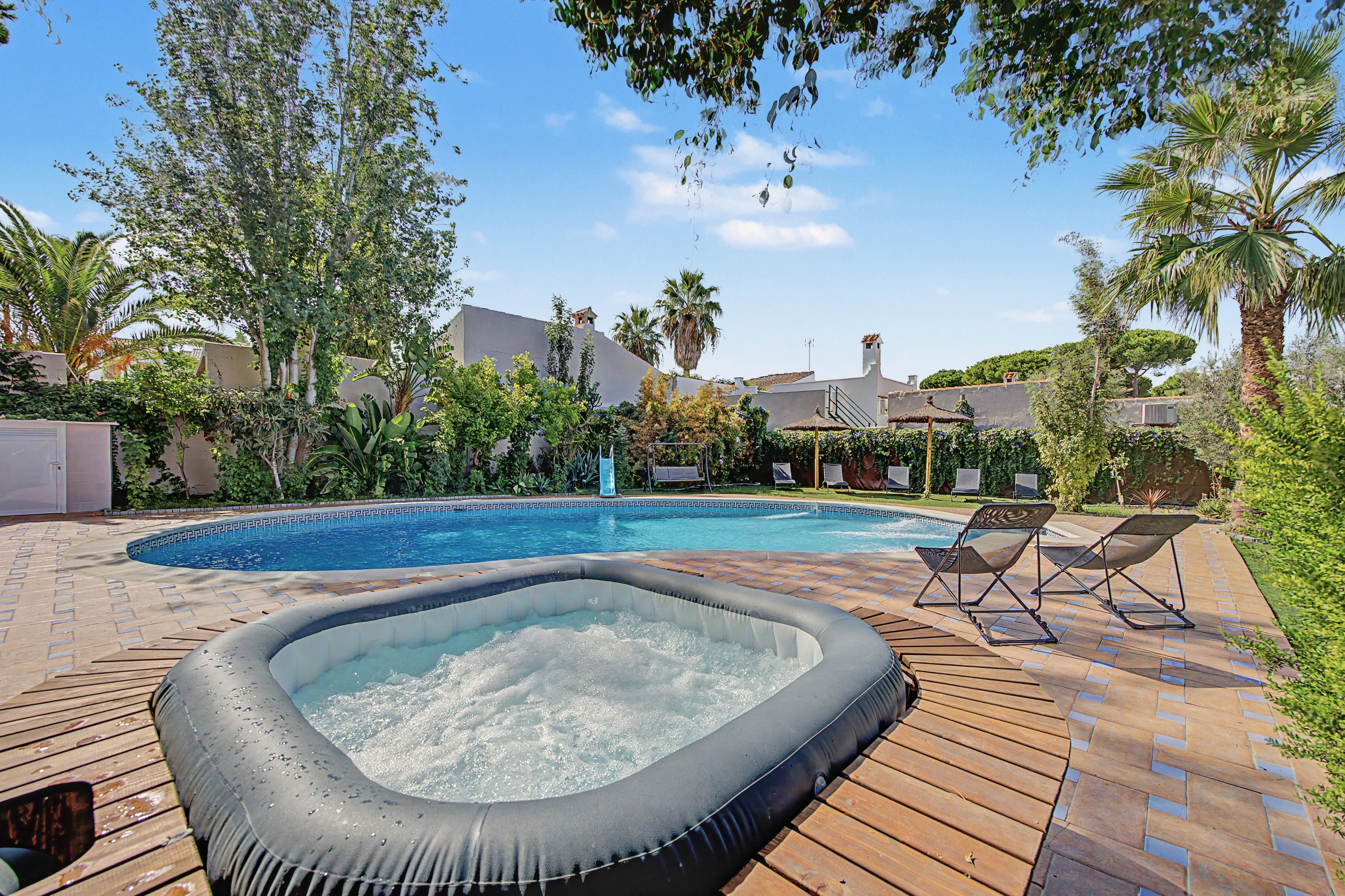 Una piscina con jacuzzi, rodeada de árboles y una terraza de madera.