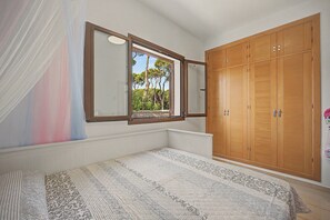 Ein Schlafzimmer mit großem Kleiderschrank, einem Bett mit gemusterten Textilien und einem Fenster mit Blick auf Bäume.