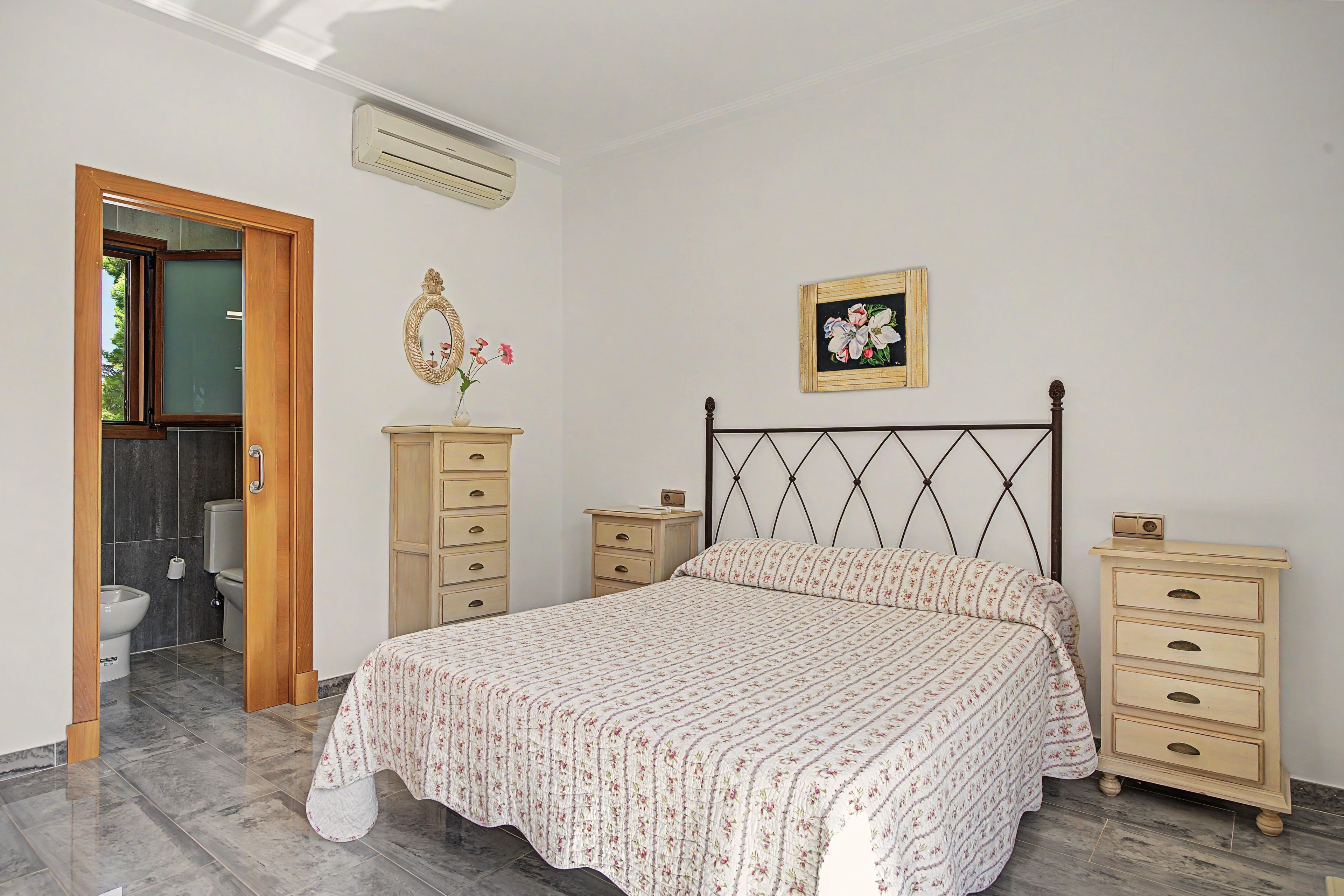 Un dormitorio con cama, cómoda, mesita de noche, espejo, marco de cuadro y unidad de aire acondicionado.