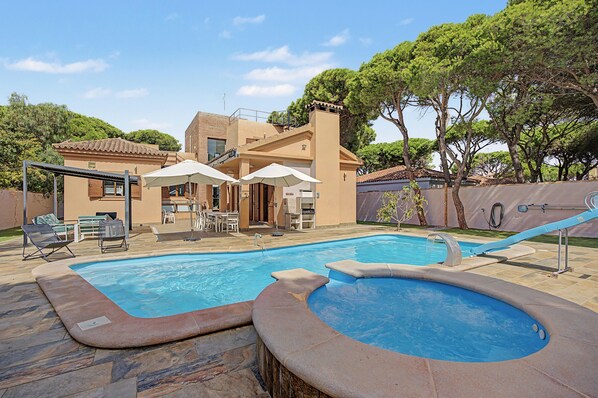Una piscina con hidromasaje, mobiliario de exterior y un patio cubierto.