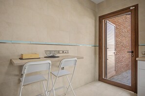 A small kitchen with a wooden countertop, two white chairs, a small table, and a brick wall visible through a door. - Holiday Home 'Villa Brasilia' with Private Pool, Wi-Fi and Air Conditioning (Chiclana de la Frontera)
