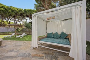 A covered outdoor seating area with a canopy, a wicker sofa with cushions, and a stone-tiled patio. - Holiday Home 'Villa Brasilia' with Private Pool, Wi-Fi and Air Conditioning (Chiclana de la Frontera)