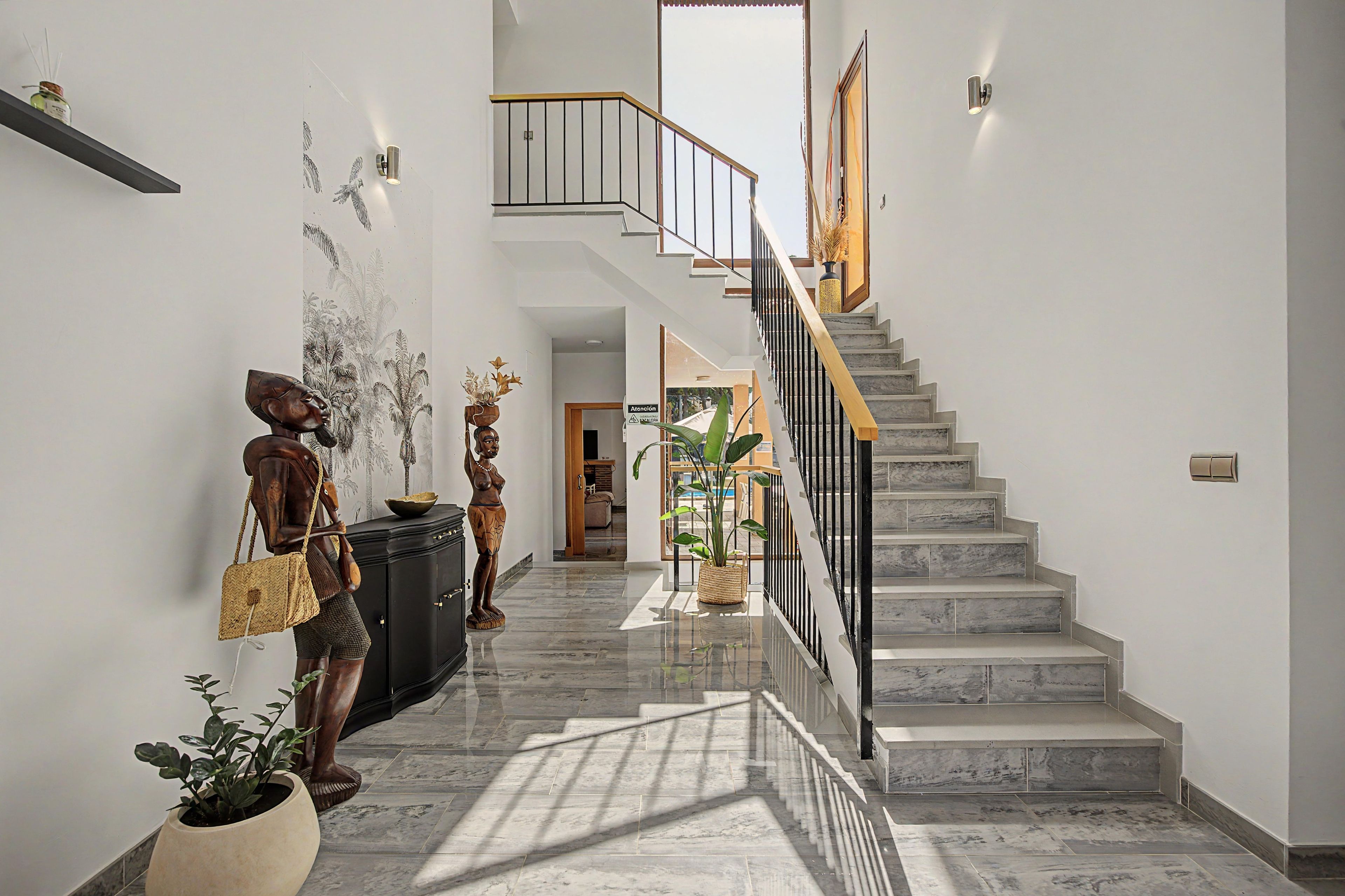 Un intérieur moderne agrémenté d’un escalier en marbre, d’un luminaire fixé au mur et d’une sculpture décorative.