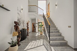 Un interior modern amb una escalinata de marbre, una làmpada penjant a la paret i una escultura decorativa.