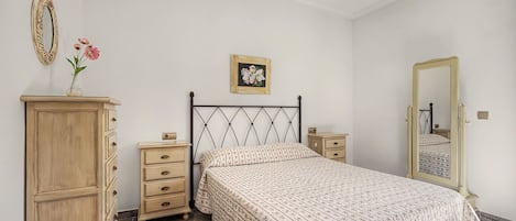 Un dormitorio con cama, cómoda, mesitas de noche, un espejo y un cuadro floral en la pared.