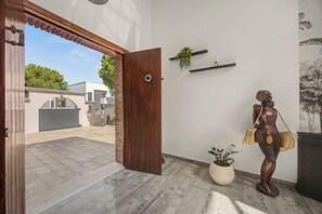Una porta de fusta oberta que dona a un pati amb terrasses i una estàtua d'una dona que subjecta un carmany.