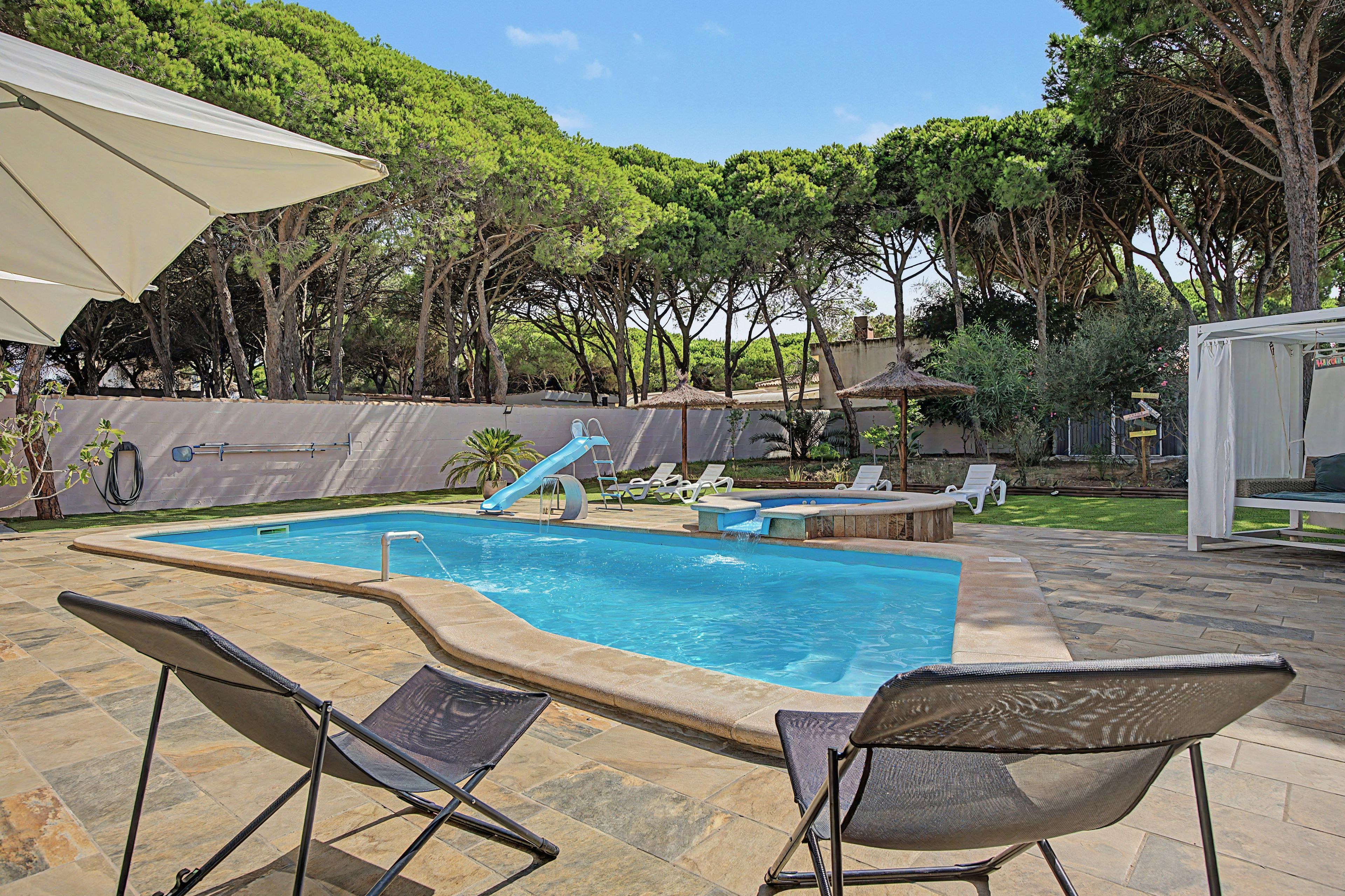 A swimming pool with a slide, surrounded by lounge chairs and a pergola.