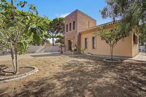Un edificio con torre de ladrillo y fachada amarilla, rodeado de árboles y una zona pavimentada.