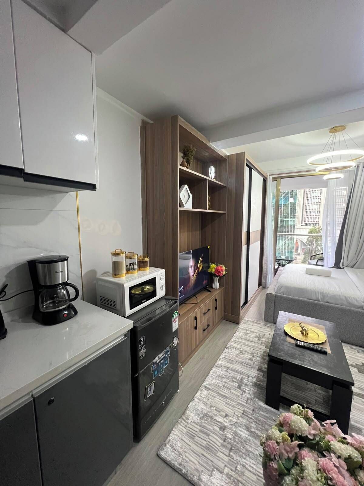 Una sala de estar moderna con una televisión de pantalla plana, una cafetera, un refrigerador pequeño y un sofá.
