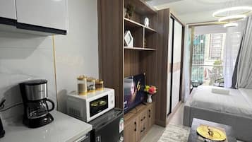 Una sala de estar moderna con una televisión de pantalla plana, una cafetera, un refrigerador pequeño y un sofá.