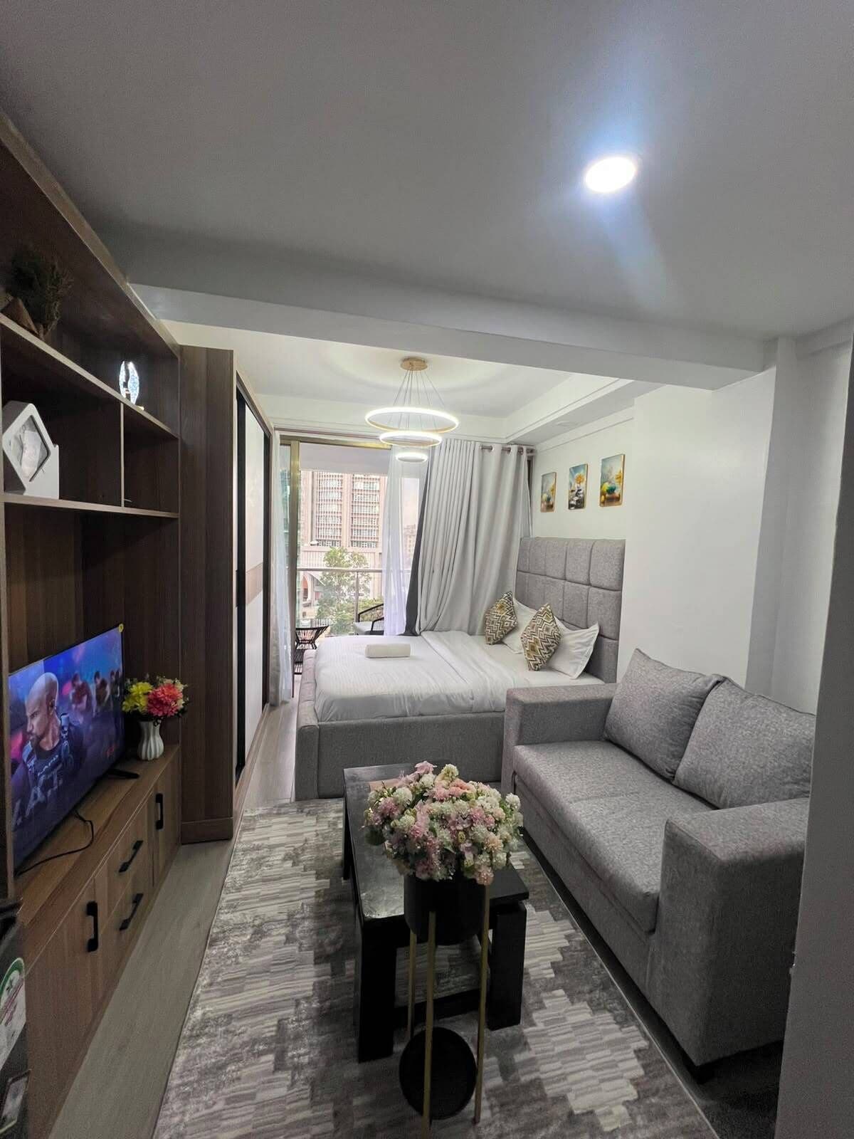 A modern living room with a sofa, a coffee table with flowers, a TV, and a bed with curtains.