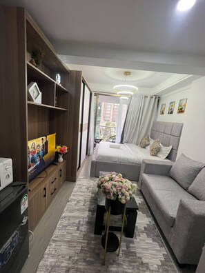 A modern living room with a sofa, a coffee table with flowers, a TV, and a bookshelf. - Gold park View Palace - Studio (Nairobi)