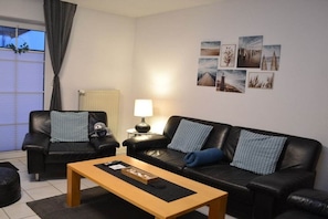 Ein Wohnzimmer mit zwei schwarzen Ledersofas, einem Holztisch, einer Lampe und einer Wand mit mehreren gerahmten Bildern.