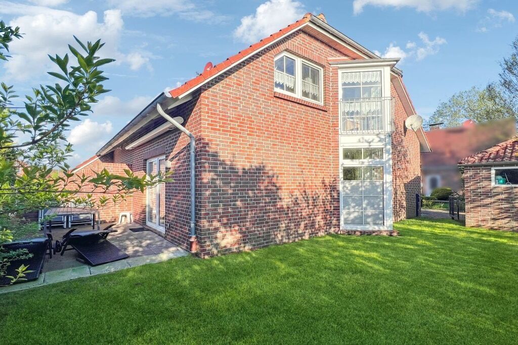 A brick house with a red roof, a glass door, and a small patio with outdoor furniture.