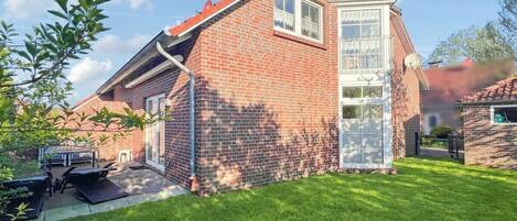 A brick house with a red roof, a glass door, and a small patio with outdoor furniture.