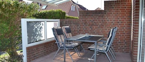 A patio with a table and chairs, a glass enclosure, and a brick wall.
