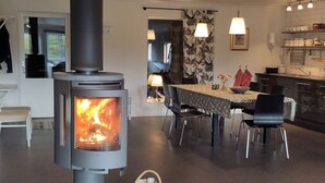 A modern interior with a wood-burning stove, a dining area with chairs, and a kitchen with cabinets. - B and B in Bjuråker with swimming pool (Bjuråker)