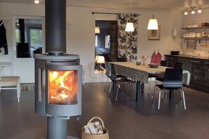 A modern interior with a wood-burning stove, a dining area with chairs, and a kitchen with cabinets.