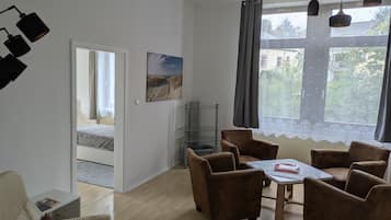 A room with a bed, a desk, a chair, a table, and a window with curtains.