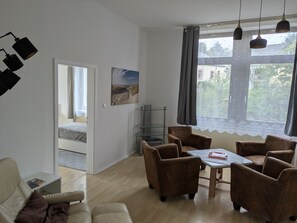 A room with a bed, a desk, a chair, a table, and a window with curtains.