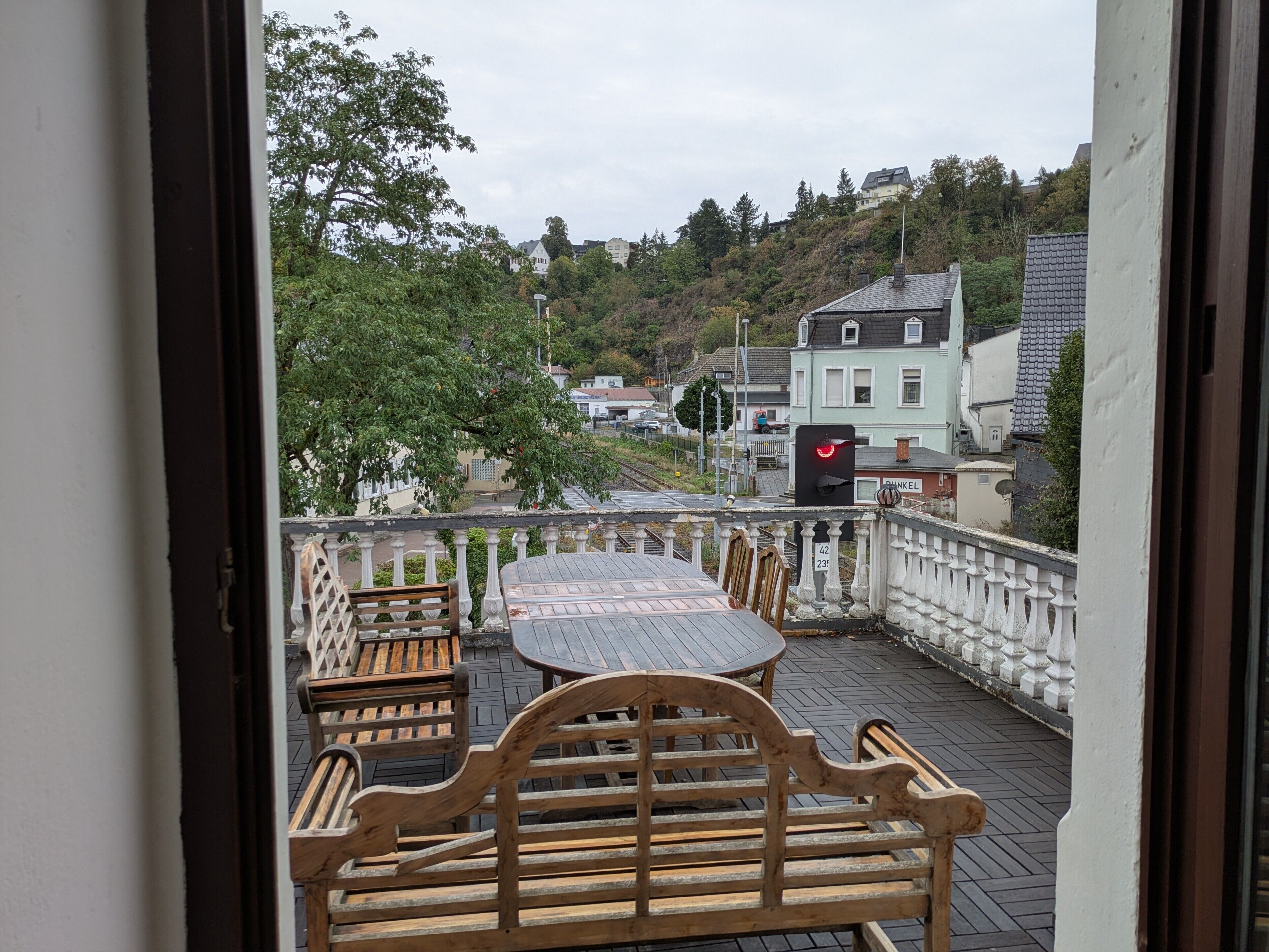 A balcony with a table and chairs, overlooking a residential area with houses and trees.