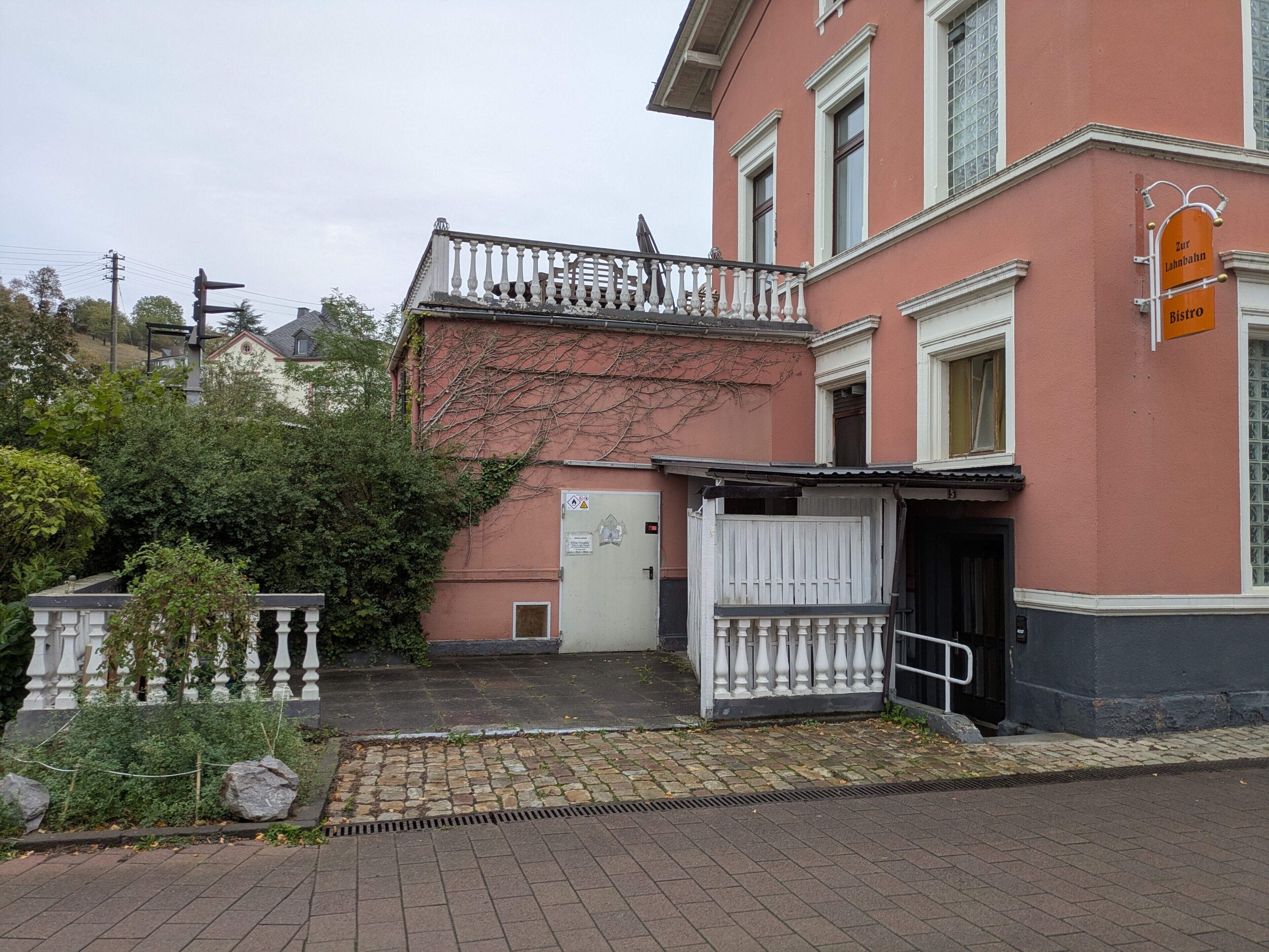 A building with a white balcony, a door, and a sign indicating a restaurant.