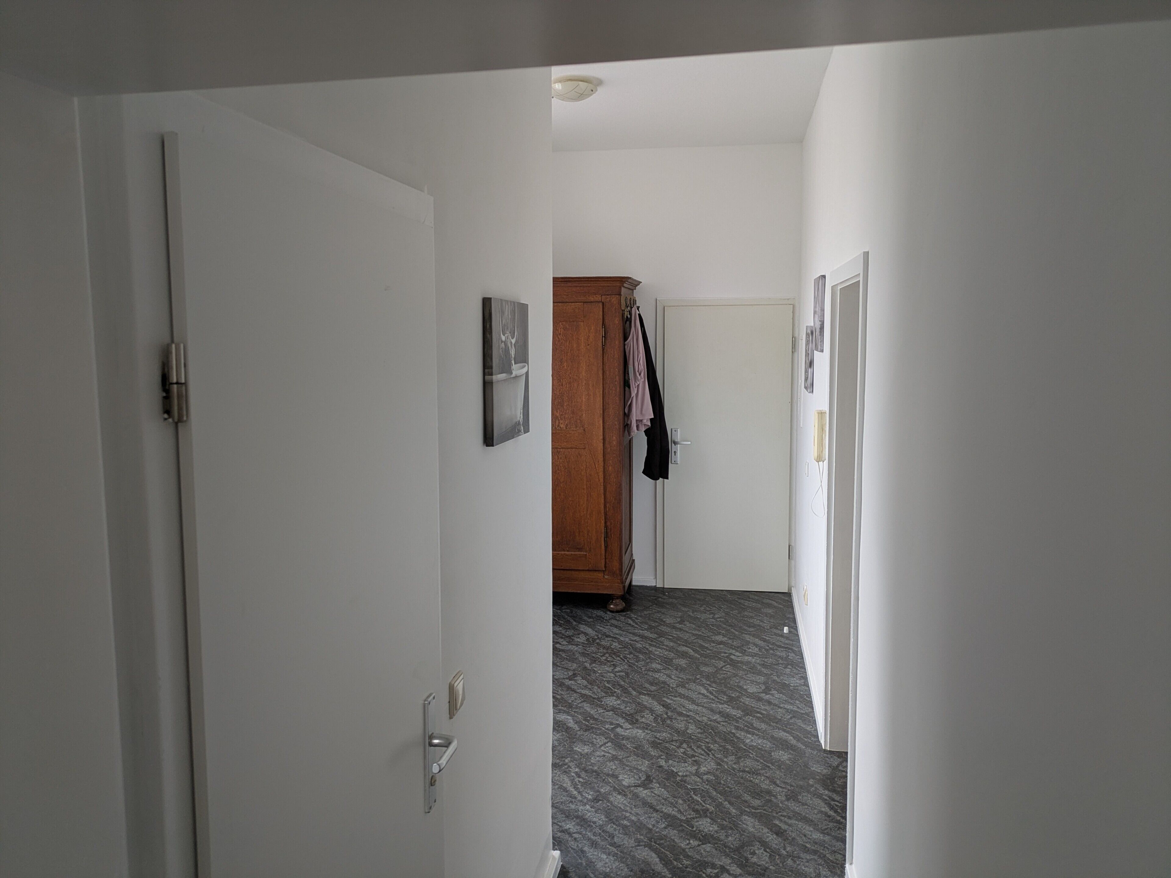 Ein Flur mit einer weißen Tür, einem Holzschrank und einem Mantel an der Wand.