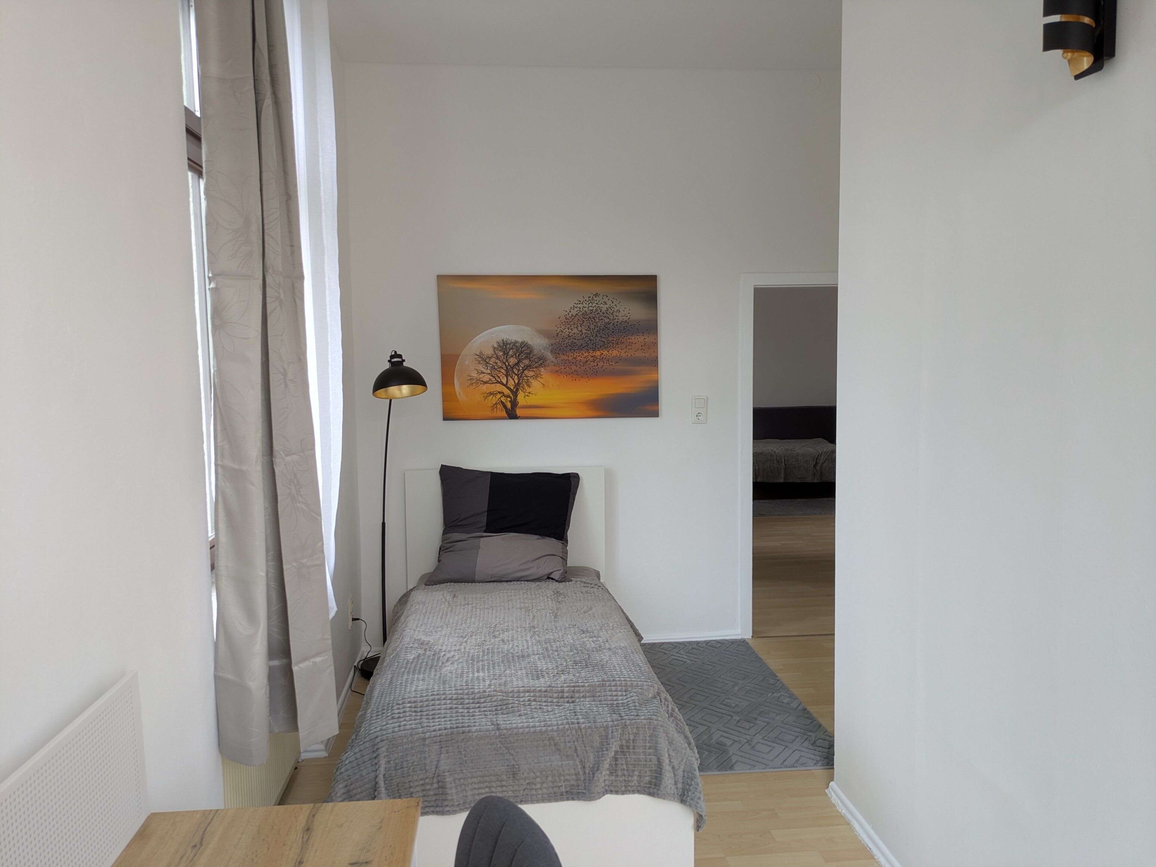 A small, modern bedroom with a bed, a bedside table, a lamp, and a painting on the wall.
