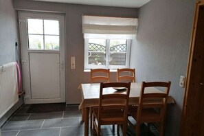 Een eetgedeelte met een tafel, vier stoelen, een raam met uitzicht en een deur.