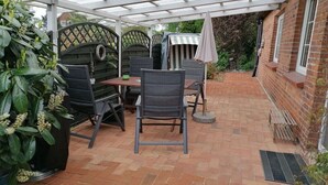 En overdækket terrasse med et bord, stole og en stribet parasol, samt en murstensvæg.