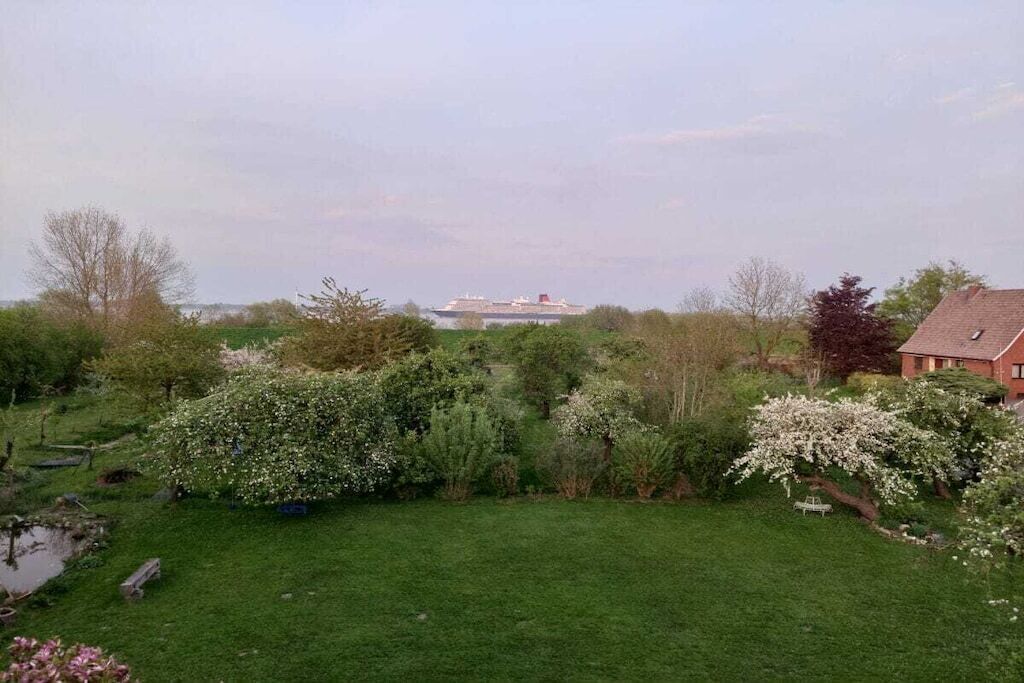 A grassy area with a body of water, trees, and a distant ship.