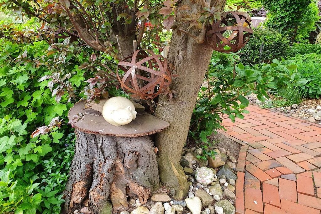 A tree stump with a white sculpture and a metal spherical ornament.