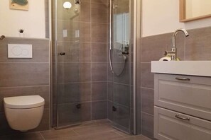 A modern bathroom with a glass shower enclosure, a toilet, and a vanity with a sink. - Semi-detached house "LUV" (Butjadingen)