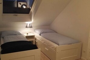 A small, single-room bedroom with two beds, a nightstand, and a window. - Semi-detached house "LUV" (Butjadingen)