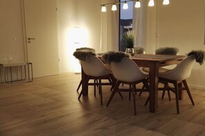 A dining area with a wooden table and chairs, a potted plant, and a window with curtains. - Semi-detached house "LUV" (Butjadingen)