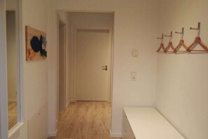 A hallway with a wooden floor, a white door at the end, and a coat rack with hangers on the right wall. - Semi-detached house "LUV" (Butjadingen)