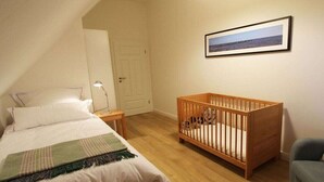Quarto com cama, berço, mesa de cabeceira, abajur, porta e quadro na parede.
