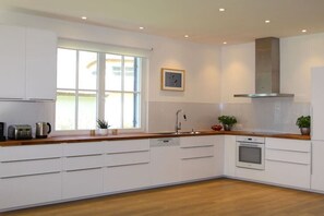 A modern kitchen with white cabinetry, a stainless steel range hood, a dishwasher, and a window providing natural light. - Holiday home in Glowe with swimming pool (Glowe)