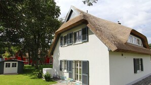 Uma casa com telhado de colmo, paredes externas brancas e persianas.