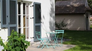 Um pátio com mesa, cadeiras, uma porta e um pequeno jardim.